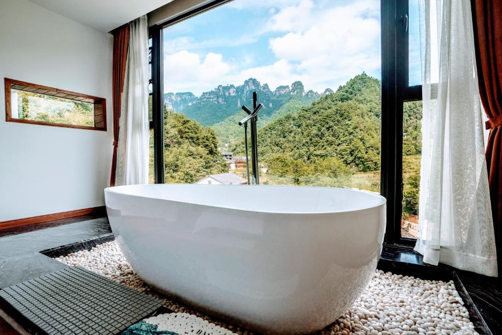 a large white bath tub in a bathroom with a window at Whispering Mountains Boutique Hotel in Zhangjiajie