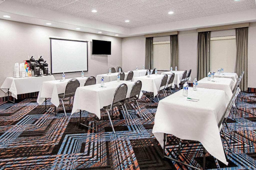 a conference room with white tables and chairs and a screen at La Quinta by Wyndham Sulphur Springs in Sulphur Springs