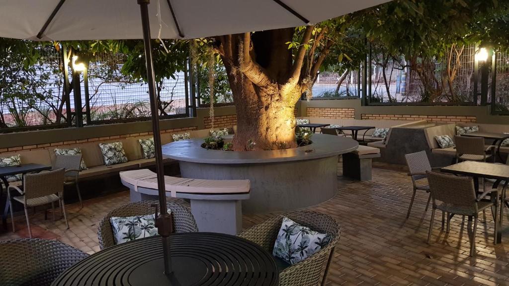 un restaurant avec un arbre, des tables et des chaises dans l'établissement Hotel das Palmeiras, à Paracatu