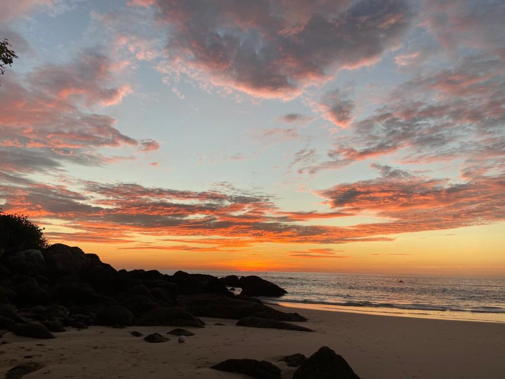 a sunset on a beach with rocks and the ocean at The Mantra Hotel Kata Noi in Kata Beach