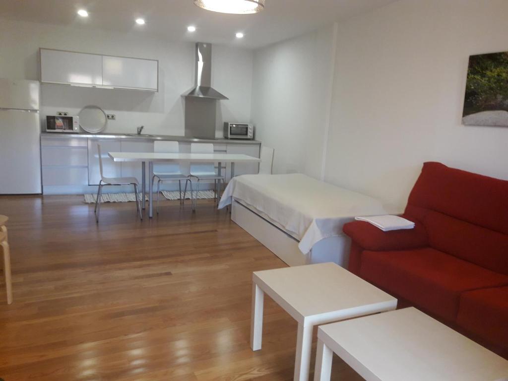 a living room with a red couch and a kitchen at Apartamentos y Estudios LA RISTRA in Jaraiz de la Vera