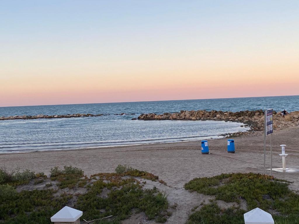 een strand met twee blauwe vuilnisbakken en de oceaan bij 1era linea de playa VILLA MARGARET Cullera Marenyet in Cullera