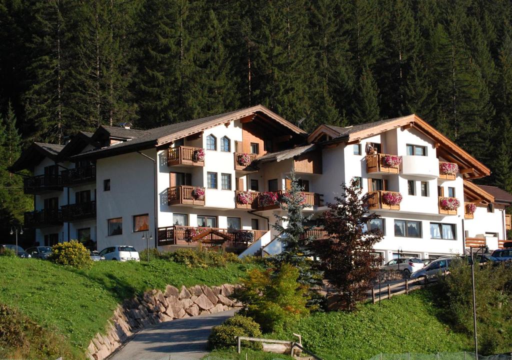 a large white building on a hill with cars parked at Hotel Terme Antico Bagno in Pozza di Fassa