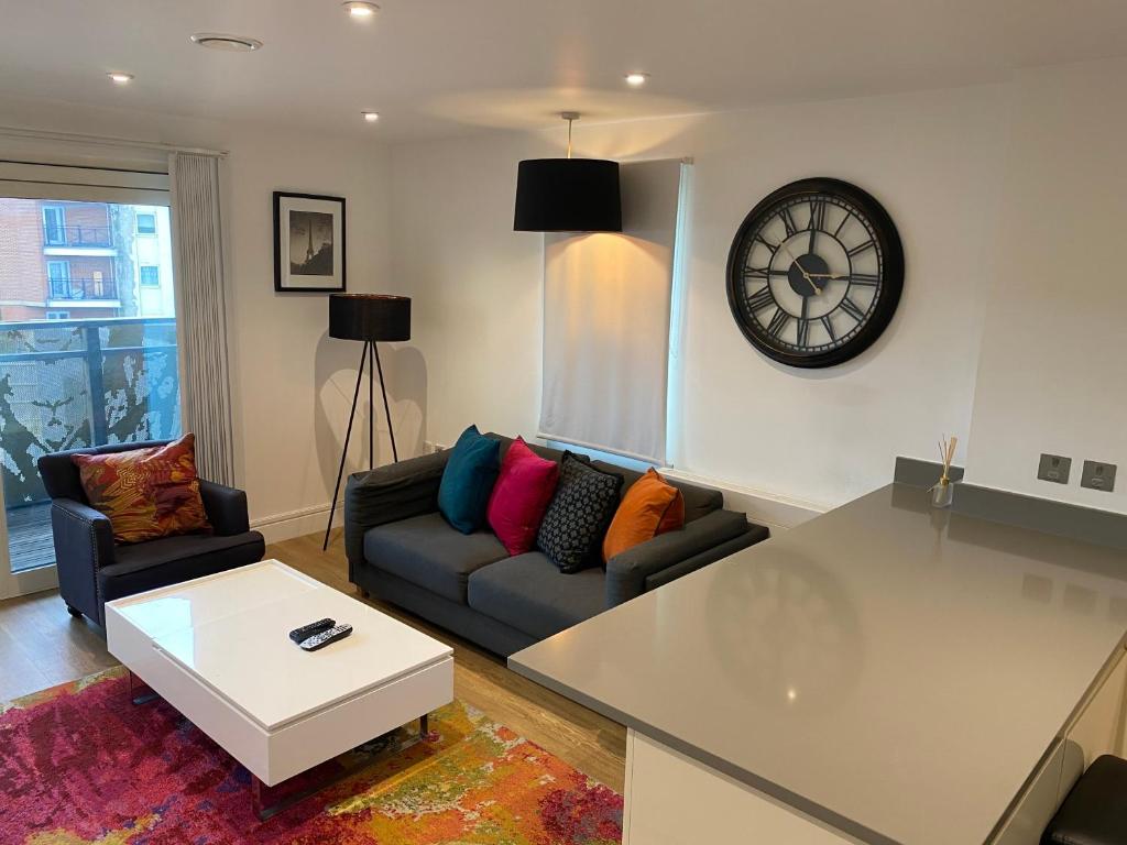 a living room with a couch and a clock on the wall at PRESTIGE 2 BED BALCONY APARTMENT in Abbey Wood
