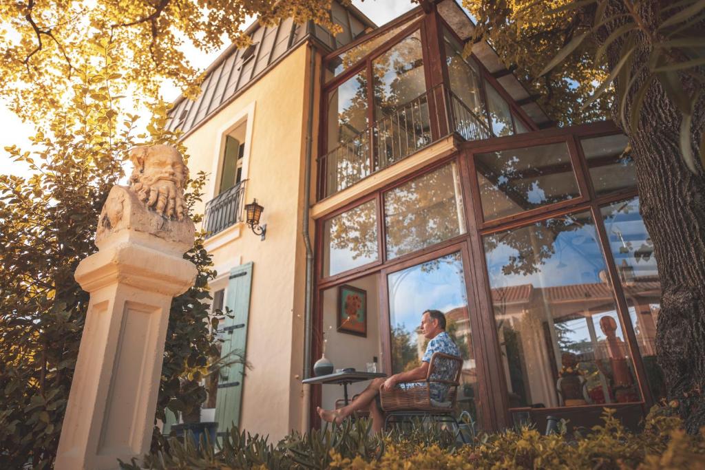 un homme assis sur une chaise devant un bâtiment dans l'établissement Villa Kumquats, à Béziers