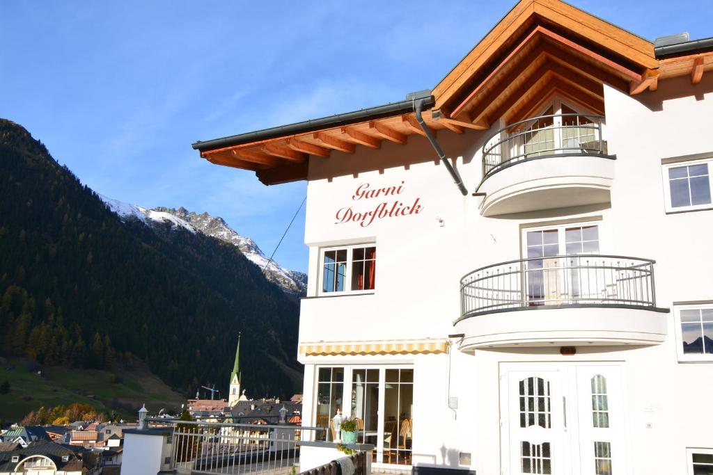 a white building with a balcony and mountains in the background at Garni Dorfblick in Ischgl