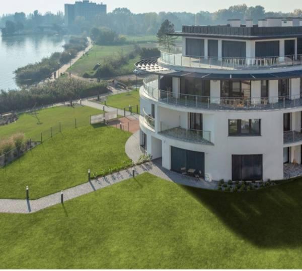 a large white building with a green lawn next to a river at Balatonparti Gyöngyszem in Keszthely