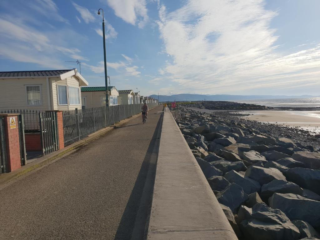 a person riding a bike down a road next to the beach at Park Home at Golden Sands Holiday Park N.Wales in Rhyl