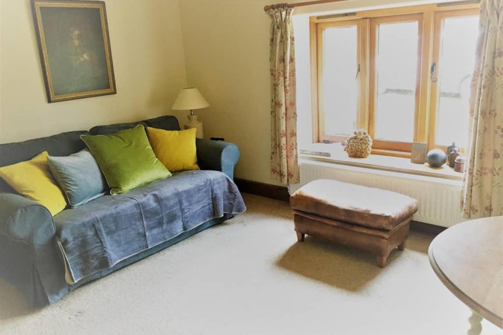 ein Wohnzimmer mit einem blauen Sofa und einem Fenster in der Unterkunft The Old Cowshed Annexe in Taunton