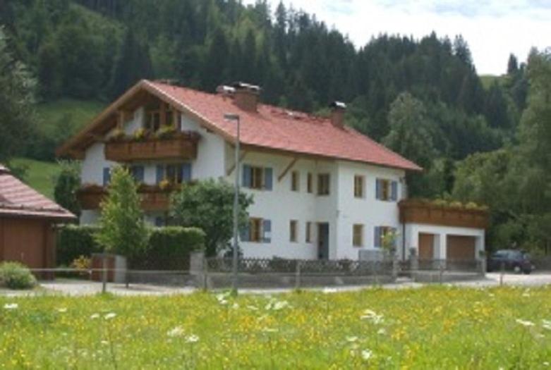 una casa blanca con techo rojo en un campo en Ferienwohnung Aletsee, en Pfronten