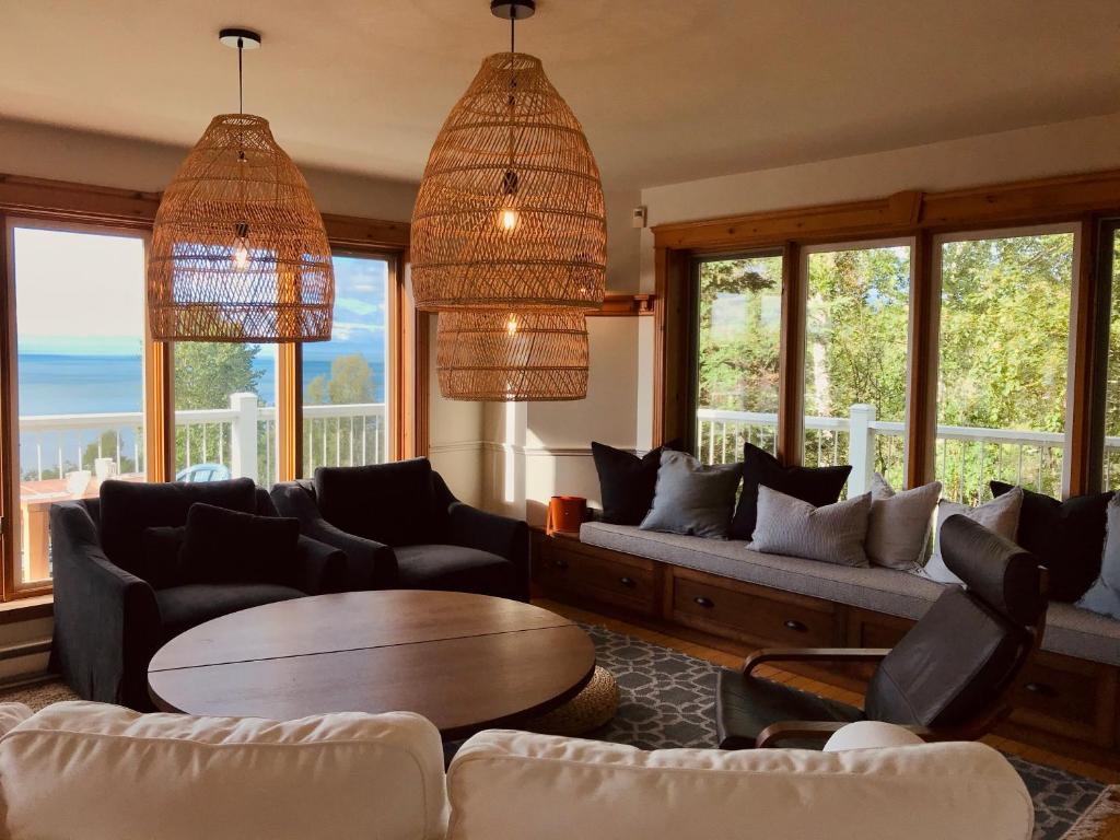 uma sala de estar com sofás, uma mesa e janelas em Auberge Cap aux Corbeaux em Baie-Saint-Paul