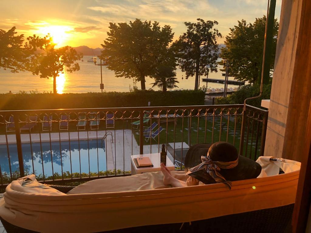 a woman sitting in a tub on a balcony with the sunset at Apartments Rainer - Front Lake in Bardolino