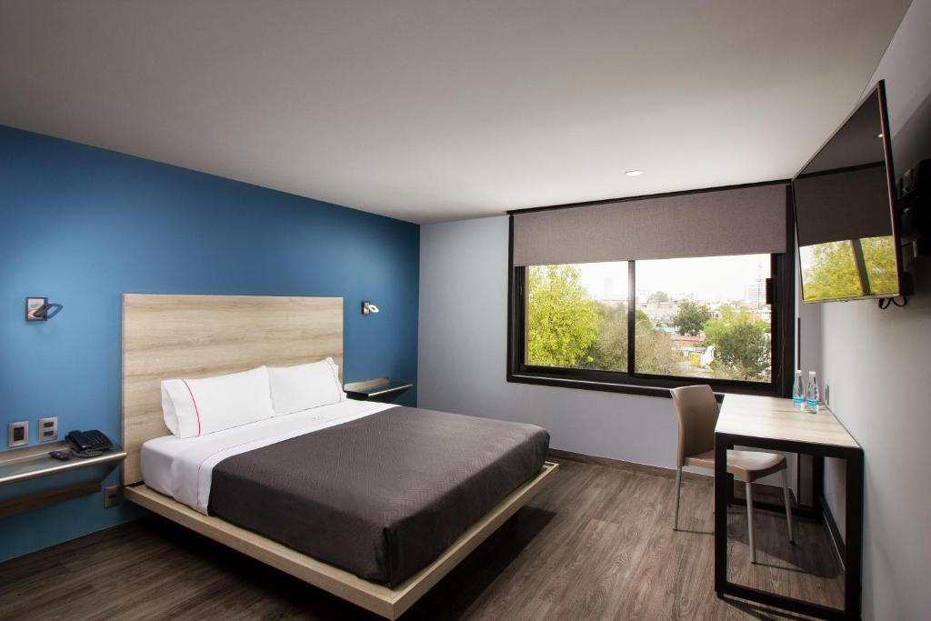 A modern guest room with one bed, a desk, and a wide window.