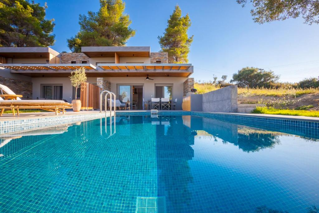 a villa with a swimming pool in front of a house at Olive White Villa in Hanioti