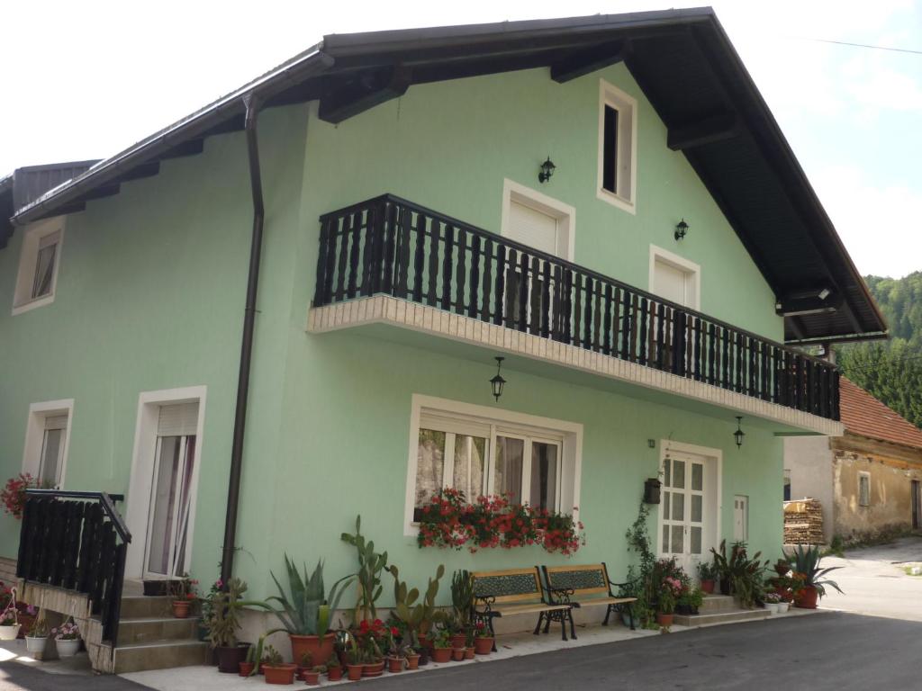 a green house with a balcony and a bench at Guest House Potok in Lokve