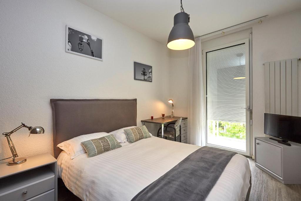 Schlafzimmer mit einem Bett, einem TV und einem Fenster in der Unterkunft Les Chambres du CTN in Genf