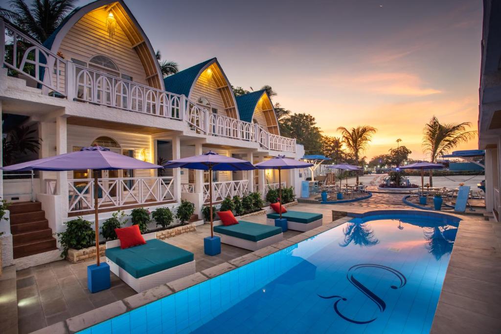 a resort pool with chairs and umbrellas at sunset at Santorini Beach Resort in Gili Trawangan