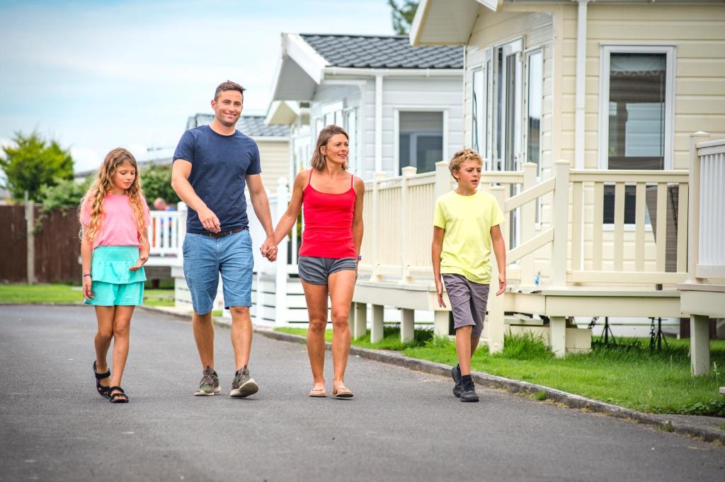 uma família a andar numa rua em frente a uma casa em Sandy Glade Holiday Park em Burnham-on-Sea