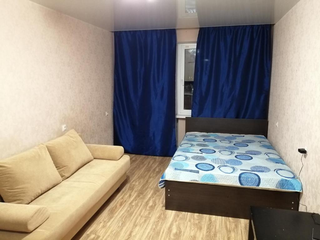 キーロフにあるОднокомнатная квартираのソファと青いカーテンが備わる小さな客室です。