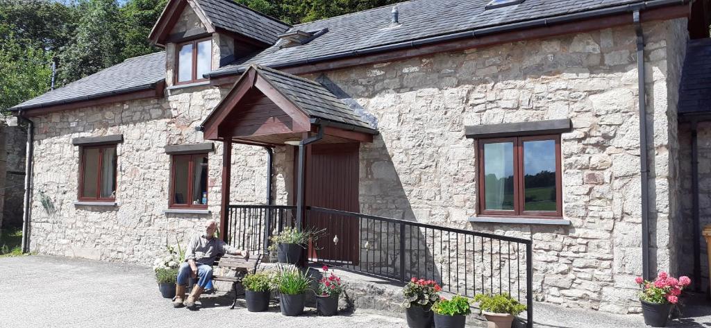 uma mulher sentada num banco do lado de fora de um edifício de pedra em Henblas Holiday Cottages em Abergele