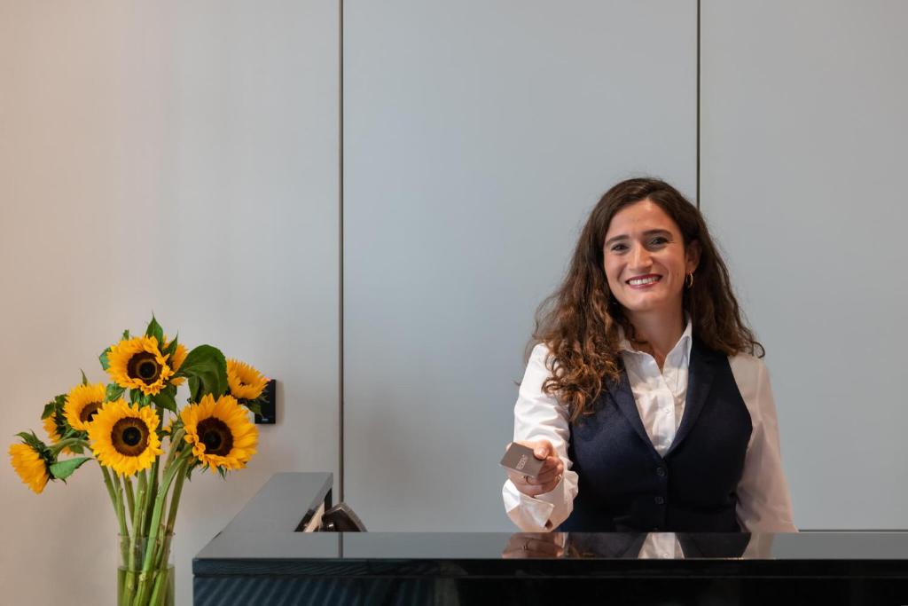 a woman standing at a desk with a vase of sunflowers at The Resident Victoria in London