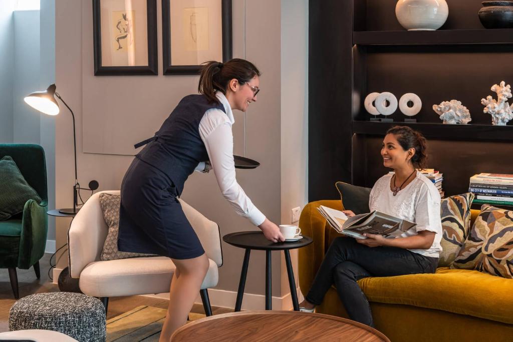 a woman standing in front of a woman sitting in a living room at The Resident Victoria in London