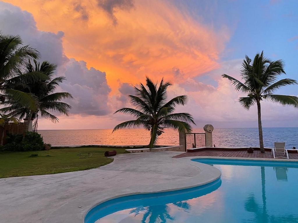 a swimming pool in front of the ocean with a sunset at Casa del Puerto by MIJ - Beachfront Hotel in Puerto Morelos