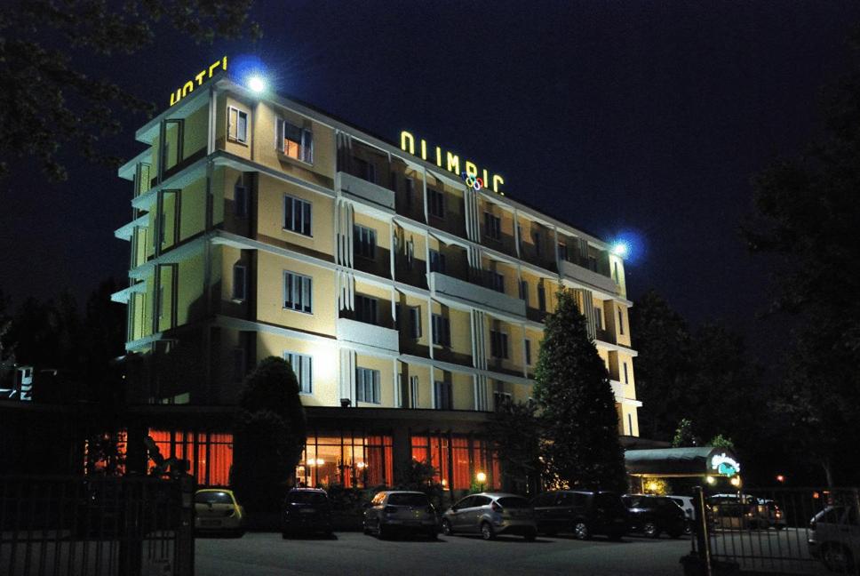 un edificio iluminado con coches estacionados frente a él en Hotel Olimpic, en Castel Maggiore