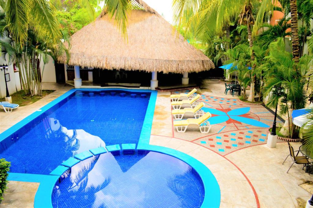 een zwembad met een rieten parasol en stoelen bij Hotel Costa Brava in Manzanillo