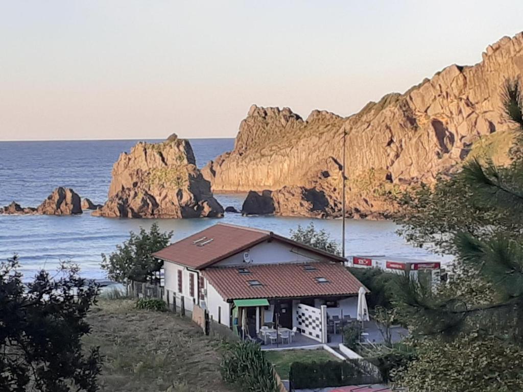 ein Haus am Meer mit Felsen im Hintergrund in der Unterkunft Playa Laga in Ibarrangelu