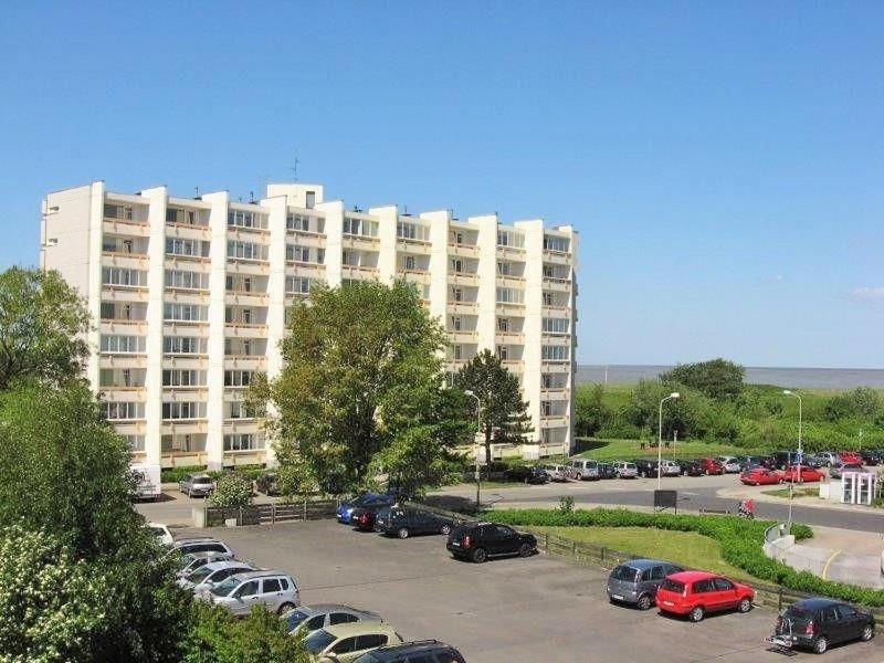 a large white building with cars parked in a parking lot at Seedeich Apartment in Cuxhaven