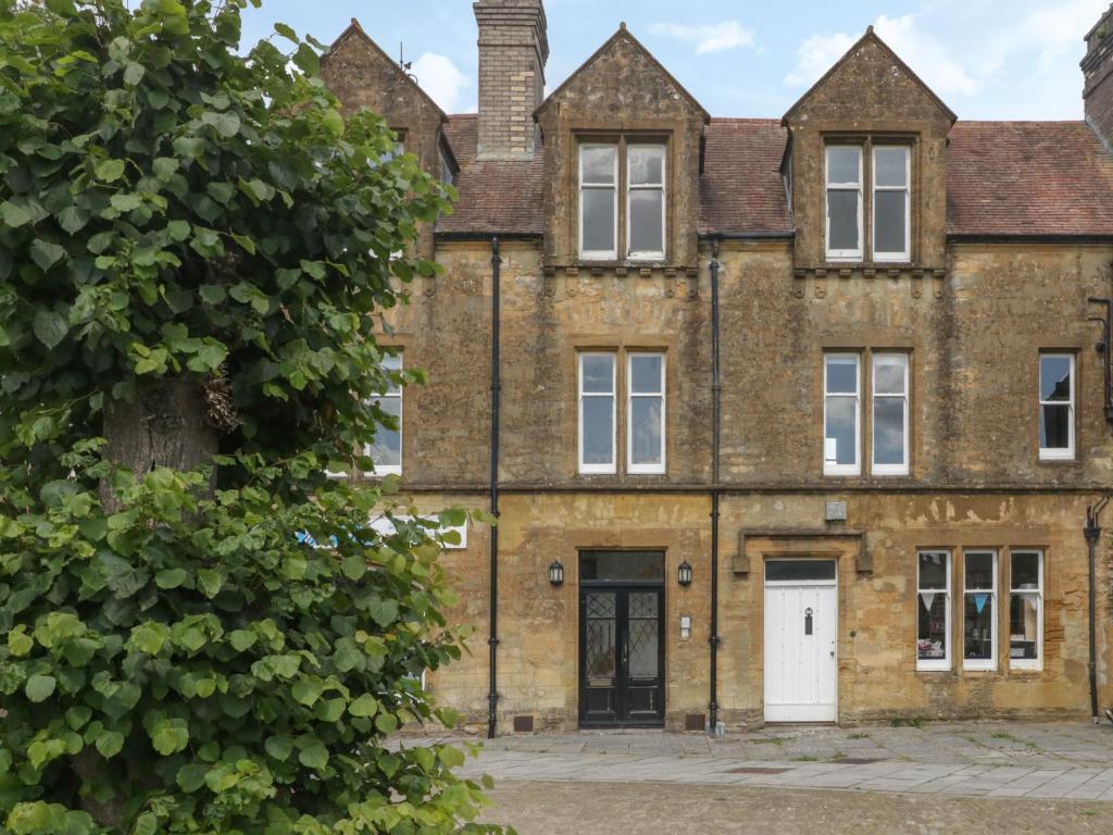 una vieja casa de ladrillo con un árbol en primer plano en 1 Abbey Court en Sherborne