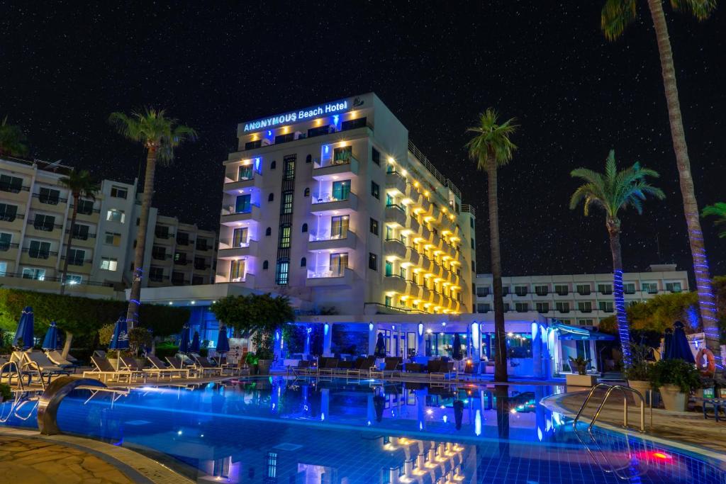 a hotel with a pool and palm trees at night at Anonymous Beach Hotel (Adults 16+) in Ayia Napa