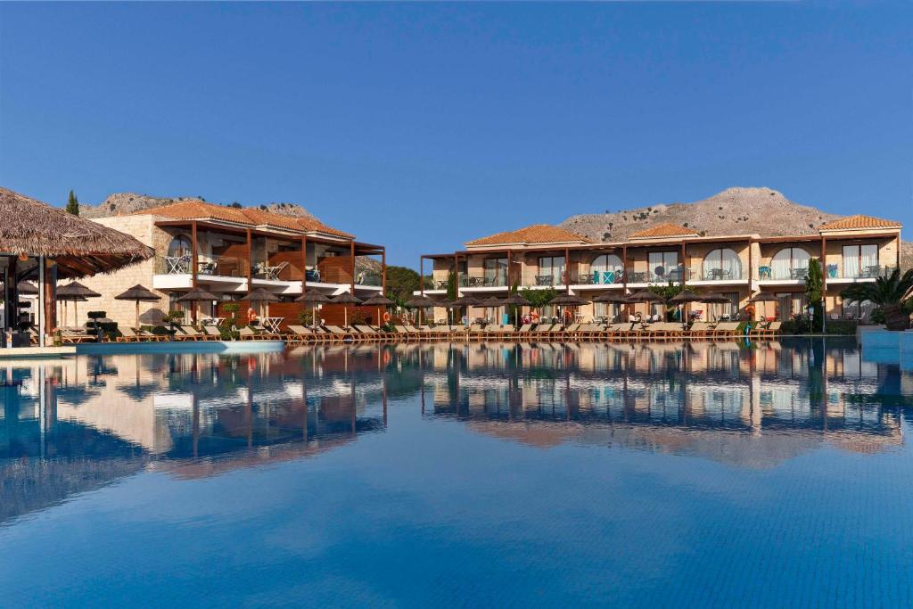 a resort with a large pool with chairs and buildings at Atlantica Holiday Village Rhodes in Kolymbia