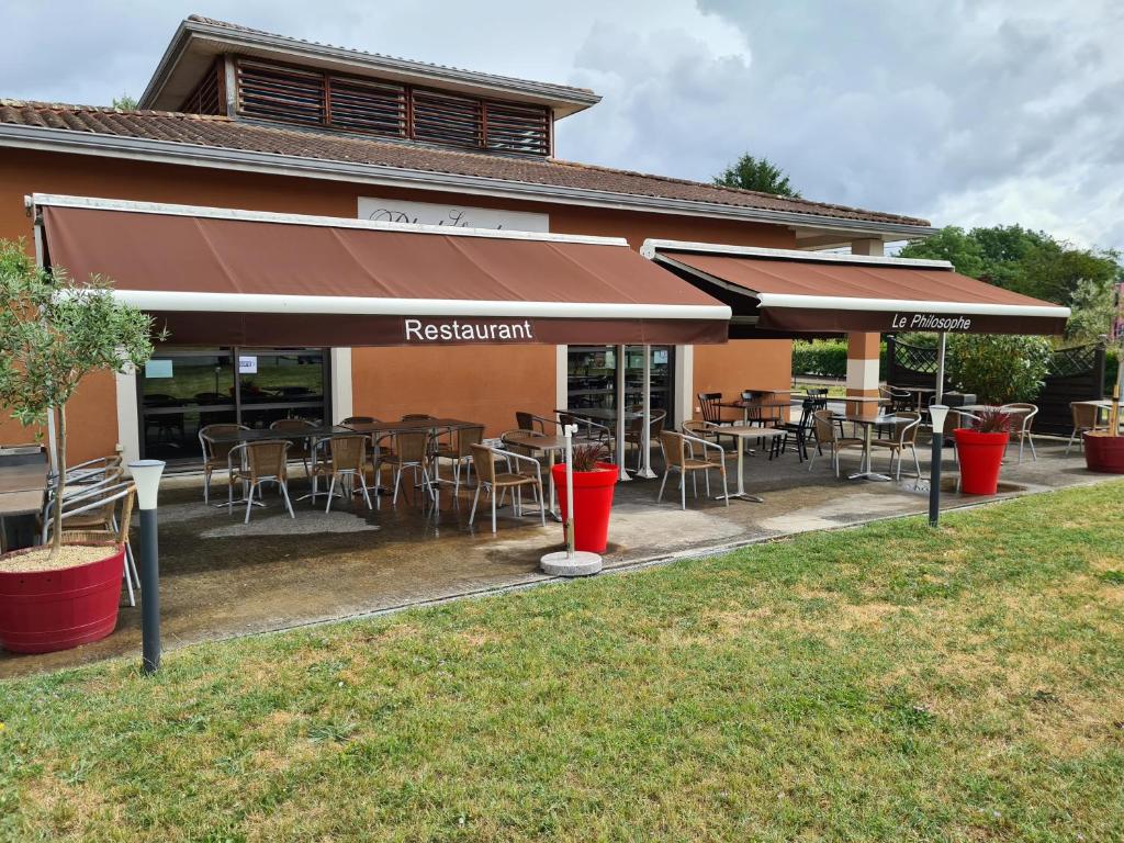 un restaurant avec des tables et des chaises en face d'un bâtiment dans l'établissement Relais Akena La Brède, à La Brède