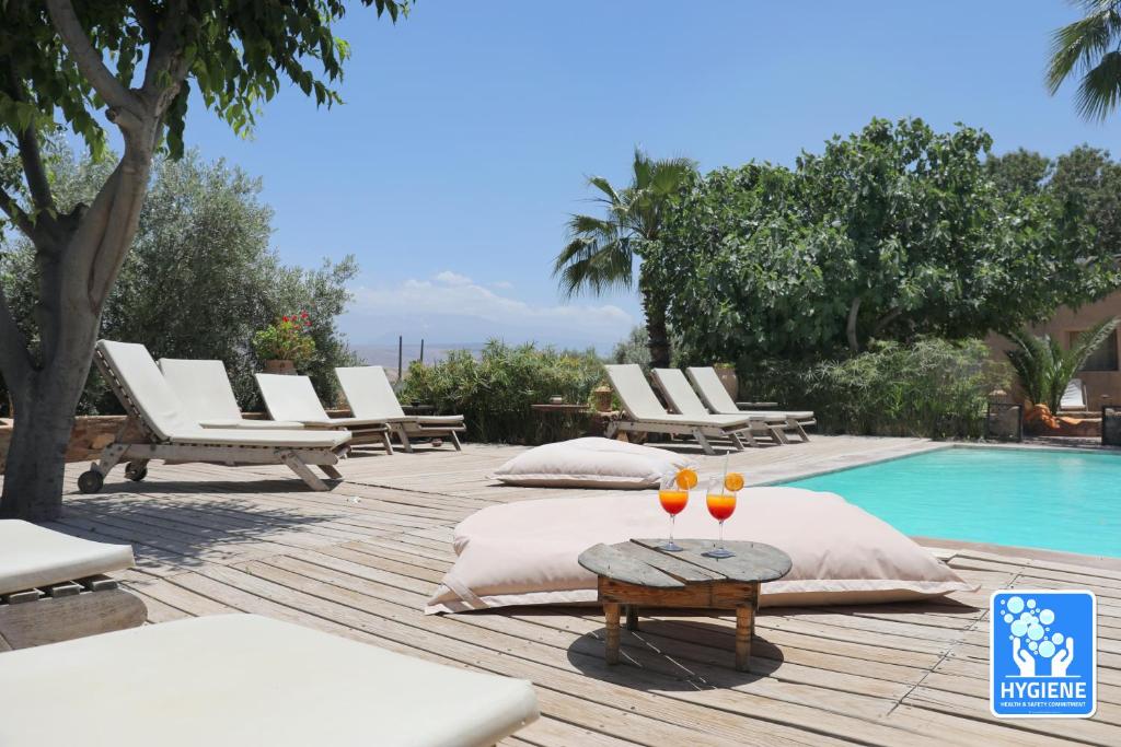 una piscina con tumbonas y 2 copas sobre una mesa en Le Petit Hôtel du Flouka, en Lalla Takerkoust