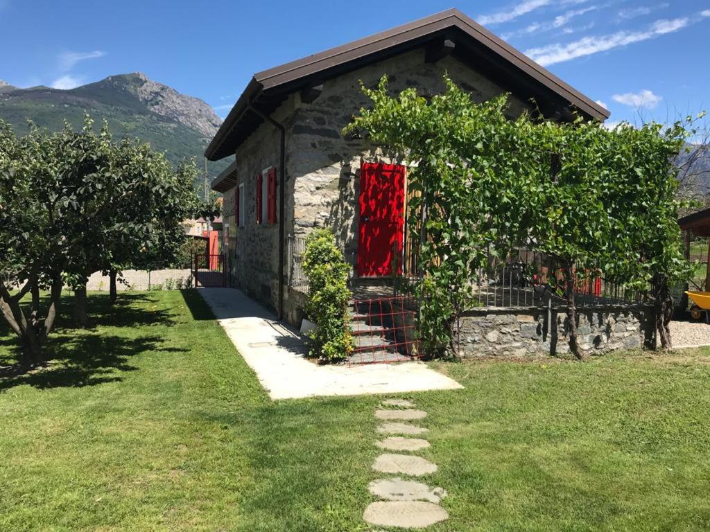 a stone house with a red door in a yard at La casetta di Biancaneve Valtellina e lago di Como in Dubino