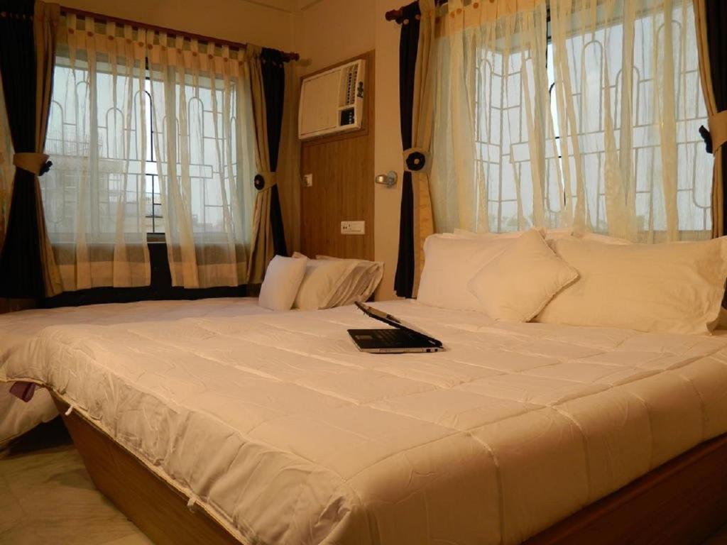 a bedroom with a large white bed with windows at The Kei Inn & Suites Hotel in Kolkata