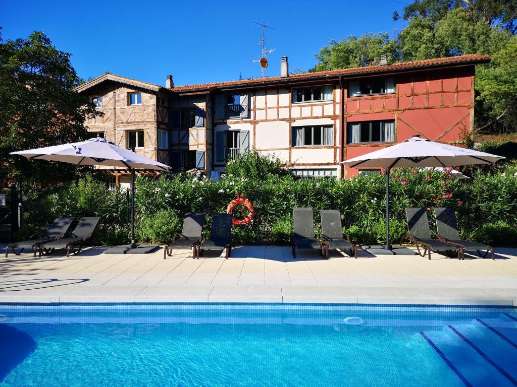 a swimming pool with chairs and umbrellas next to a building at Hotel Zubieta in Lekeitio