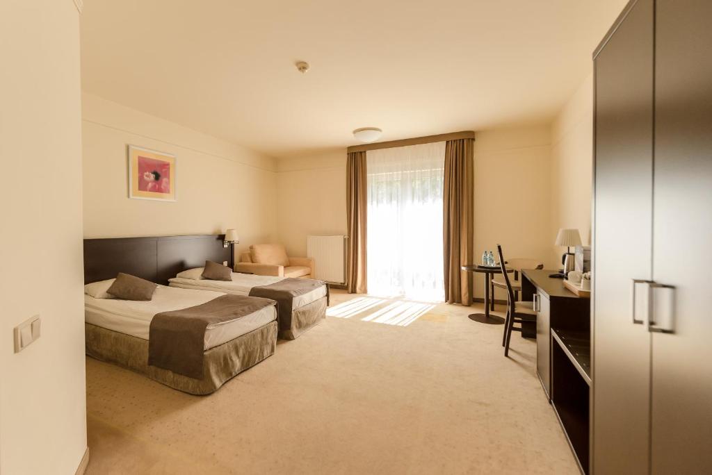 Spacious hotel room with two twin beds, desk and seating area, sunlight streaming through balcony