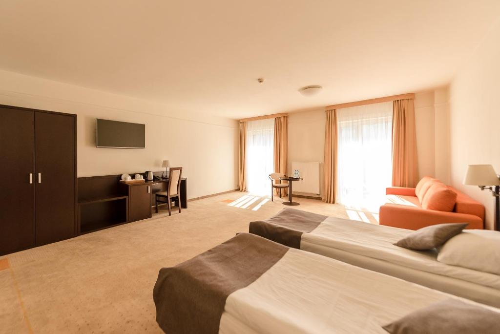 Bright hotel room with twin beds in foreground, wardrobe, desk and orange sofa by windows