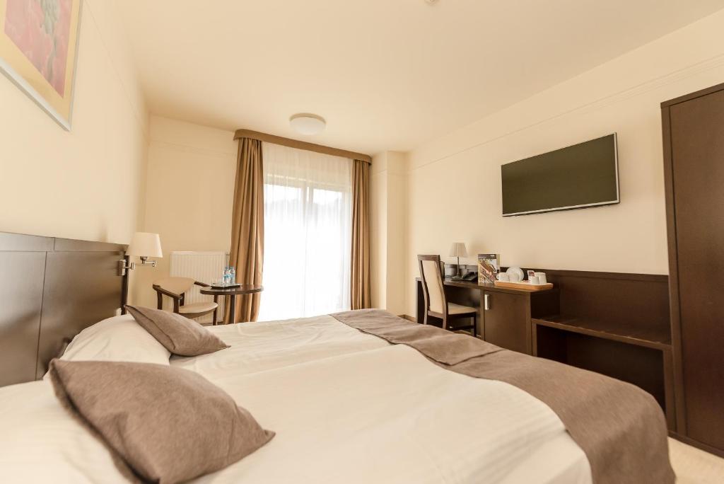 Pair of neatly made beds with brown runners, small table and TV, softly lit.