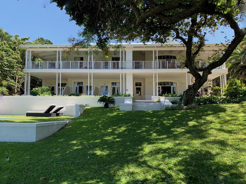 a large white house with a tree in the yard at Coral Tree Colony Bed & Breakfast in Southbroom