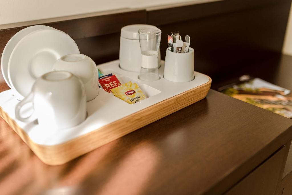 Tea and coffee tray with white cups, glass, sugar packets and stirrers on wooden surface.