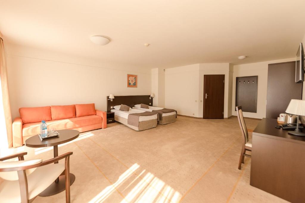 Large airy hotel room with twin beds, orange sofa, small round table and sunlight patterns