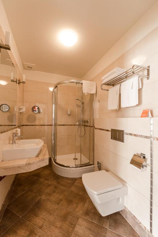 Compact hotel bathroom with glass corner shower, wall-mounted toilet and sink with mirror