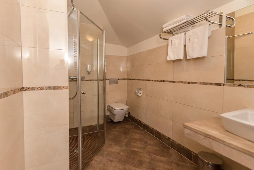 Spacious beige-tiled bathroom with glass shower enclosure, wall-mounted toilet, sink and towel rack.
