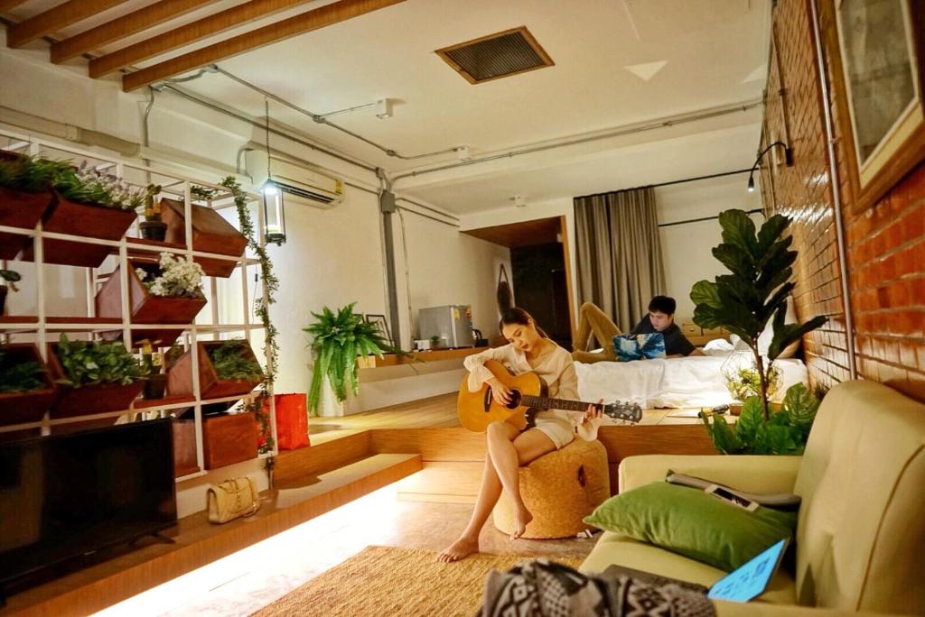 una mujer sentada en un sofá tocando una guitarra en una sala de estar en Hidden Habitat - Design Guesthouse, en Bangkok