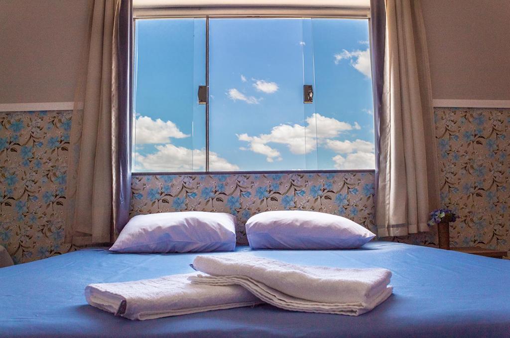uma cama com duas toalhas com uma janela em Pouso Oliveira Suítes em São João Batista do Glória