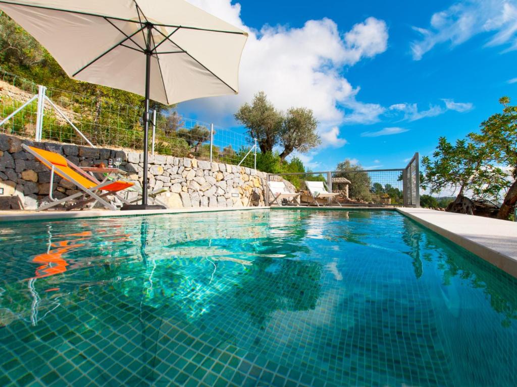 a swimming pool with an umbrella and a chair and a swimming pool at Villa Mancor Pool & Mountain Views in Mancor del Valle